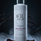 OL Skincare Replenishing Rose Facial Sprayer bottle, presented on a dark stone pedestal with rose petals and smoke against a dark background.